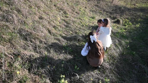 Three Young Girls Explore a Grassy Hillside on a Sunny Day, Discovering Nature Together in a Serene Outdoor Setting, Capturing the Innocence and Joy of Childhood Play