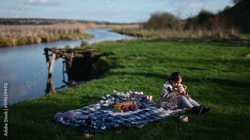 Happy Little Girl Enjoys a Peaceful Picnic by the River, Sipping from a Cup and Smiling Joyfully in Nature.