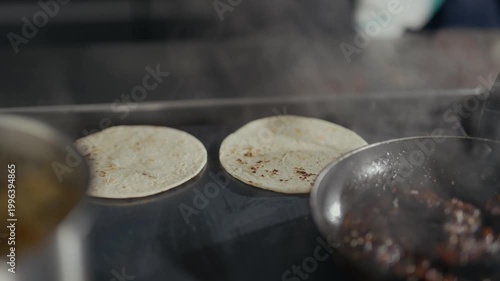 Steam rises from a hot griddle. Hands place tortillas carefully on the surface. Cooking process is shown with precision. Tortillas sizzle, creating a warm, aromatic scene. Ideal for food, restaurant