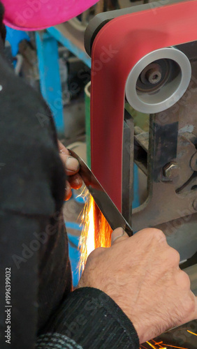 Blacksmith grinding a Damascus steel blade with sparks flying in a workshop.