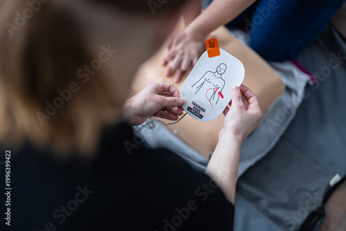 Person performs CPR chest compressions on training mannequin during first aid class. AED pads and rescue equipment lie nearby, highlighting emergency response skills and lifesaving practice.