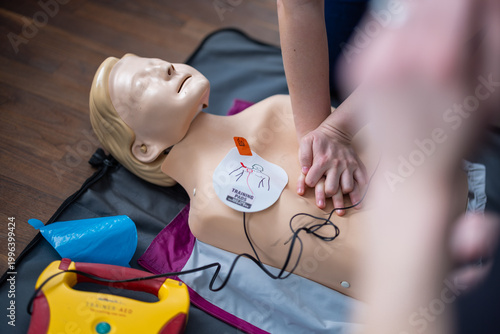 Person performs CPR chest compressions on training mannequin during first aid class. AED pads and rescue equipment lie nearby, highlighting emergency response skills and lifesaving practice.