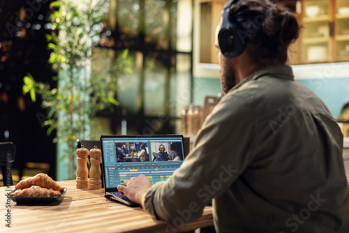 Man editing video clips and sound effects with headset at laptop, videography and post production with cinematic color grading. VFX elements and interactive software, professional content creator.