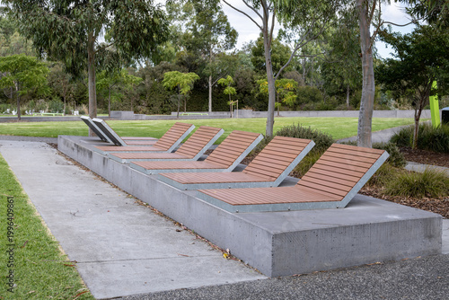 Photography A row of modern slatted reclining sun lounger seats on a concrete plinth in a leafy suburban parkland in Melbourne, Australia