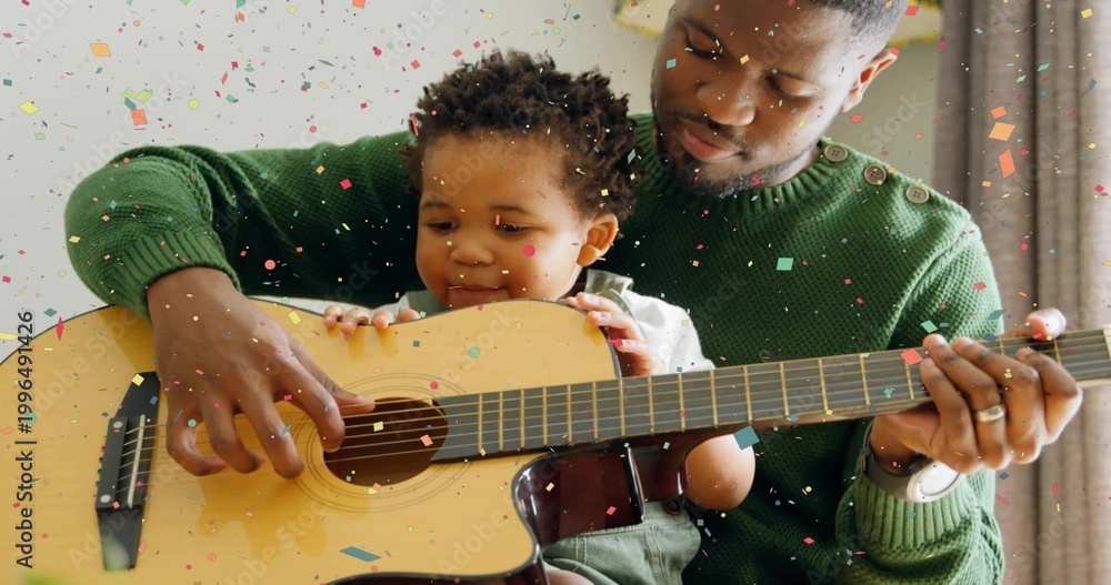 Fototapeta premium Playing father and baby guiding hands on home sofa with wood guitar, green sweater, green overalls