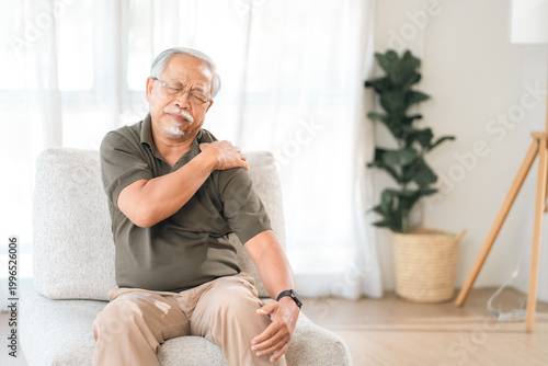 Foto Elderly man shoulder pain sitting on chair in bright living room, painful postur
