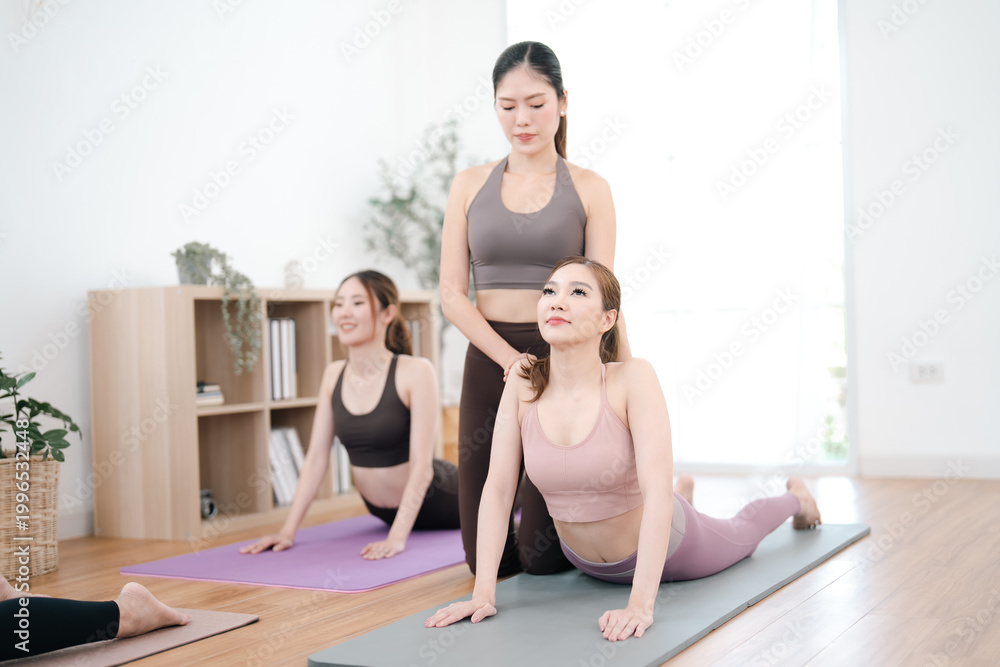 Obraz premium Yoga class with three women in studio, stretching on mat with instructor guidance and calm focus