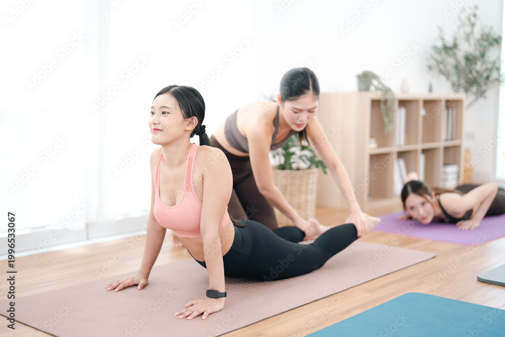 Obraz premium Yoga class with female instructor assisting woman on mat in bright studio, wellness and flexibility practice