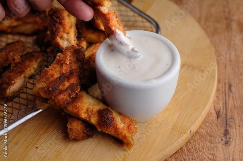 Milanesas de pollo pescado o camarones empanizados con un tazoncito de ranch o gravy para sazonar, sobre una tabla de cortar de madera