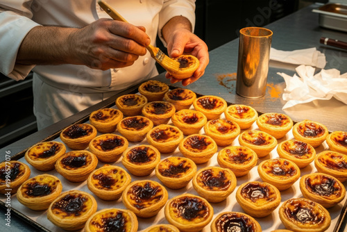 Pastry chef brushing freshly baked Portuguese egg tarts on a tray in a professional bakery kitchen
