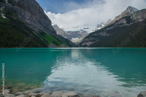 Stunning summer landscape of the turquoise Lake Louise in Banff National Park, Alberta, Canada. Majestic Rocky Mountains with snow-capped peaks and evergreen pine forests reflecting in the water below