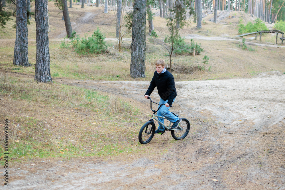 Fototapeta premium Teenage Boy Riding BMX Bike on Dirt Trail in Pine Forest Outdoor Activity and Extreme Sport