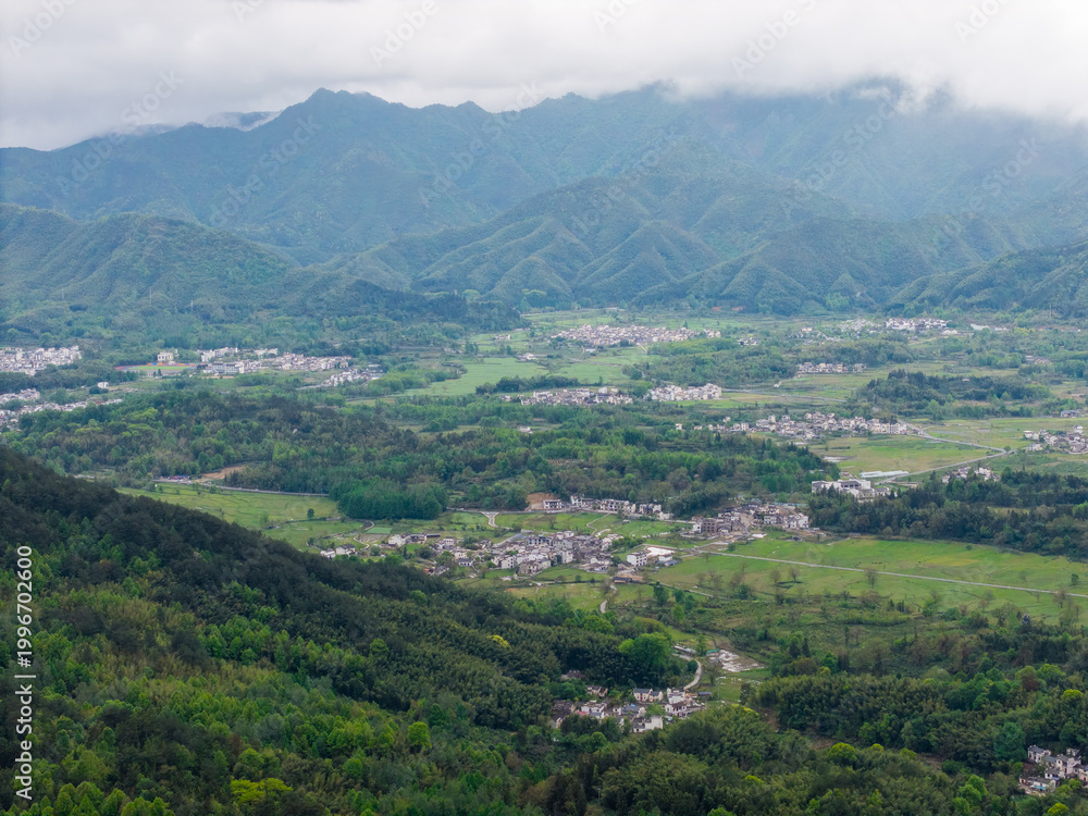 Fototapeta premium A panoramic aerial view displays the ancient Hongcun Village nestled within the green mountains of Yixian County in Anhui China with traditional architecture surrounded by lush fields and hills