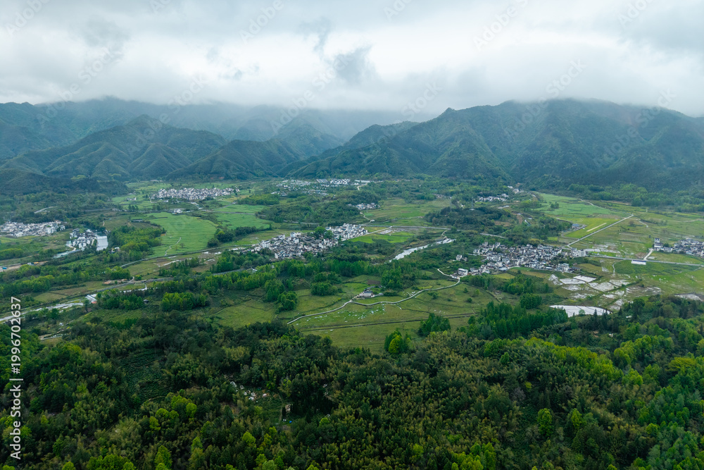 Obraz premium An aerial view captures the traditional architecture of the ancient Hongcun Village located in Yixian County of Anhui Province in China surrounded by lush green mountains and vast agricultural fields