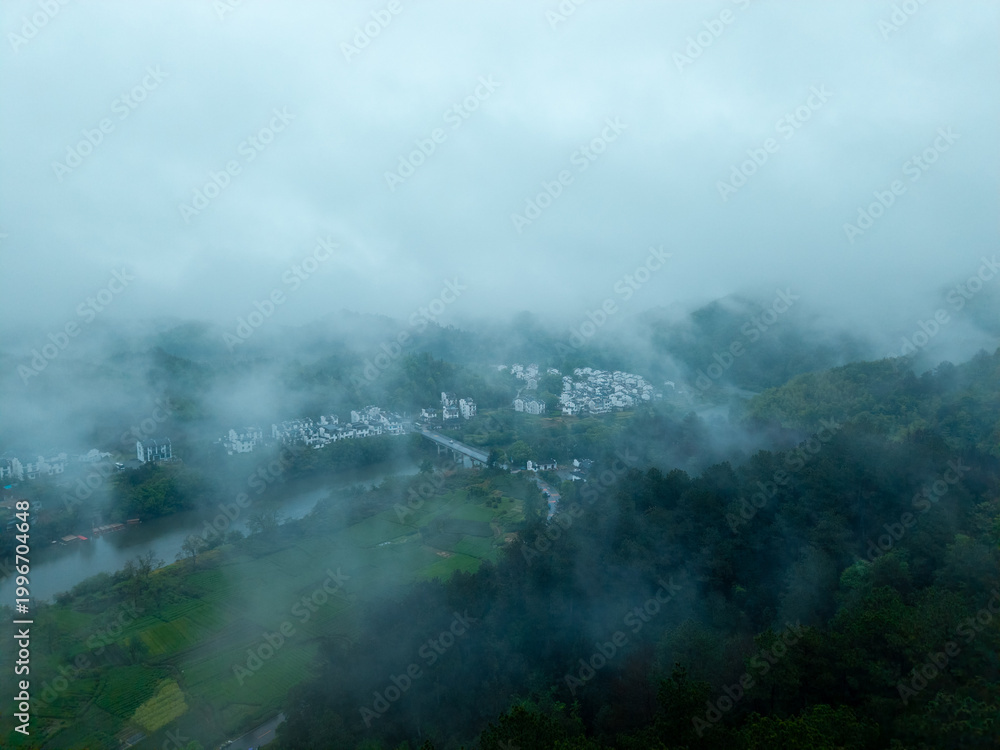 Fototapeta premium A high angle view captures the ancient Huizhou City located in She County of Anhui Province in China as it sits surrounded by green mountains and thick morning fog during the day