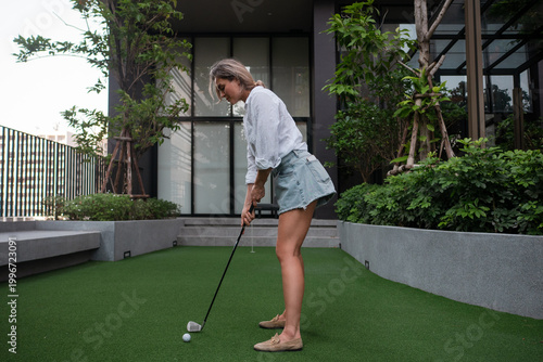 Woman putting golf ball on private green in modern residential courtyard