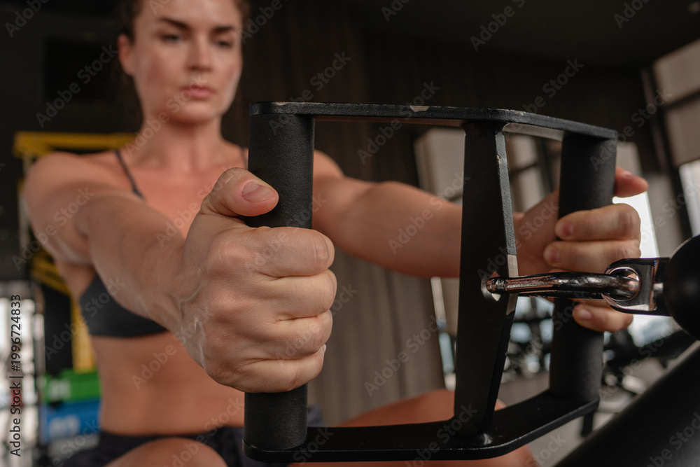 Fototapeta premium Athletic woman performing seated cable row exercise in gym