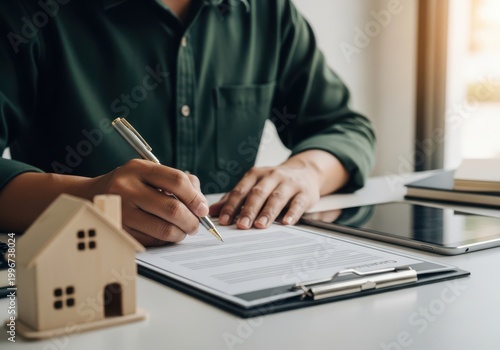 Person signing documents with a miniature house model nearby