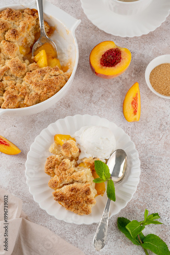 Homemade summer peach cobbler. Pie with juicy peaches, a scoop of vanilla ice cream and fresh mint on a white plate. Comfort food.