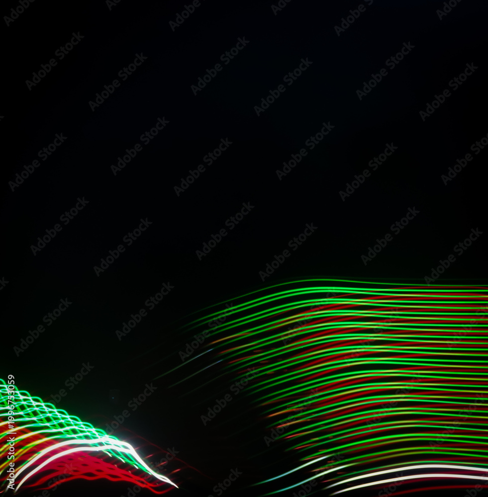 Obraz premium Long exposure light painting featuring vibrant red and green wavy lines flowing across a dark black background.