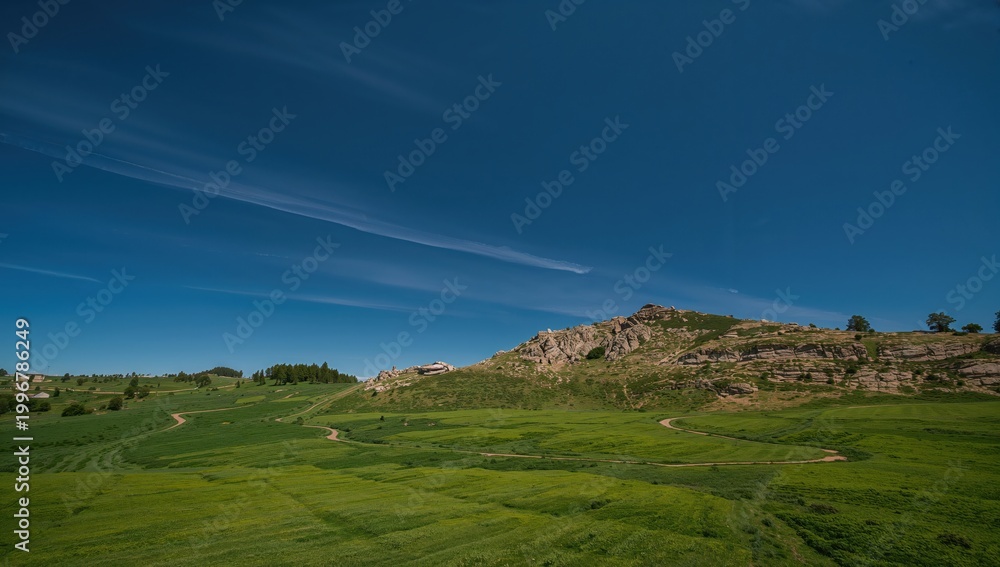 Fototapeta premium Narrow winding white path through open green hillside with rocky cliff and clear deep blue sky scenic nature landscape photography editorial