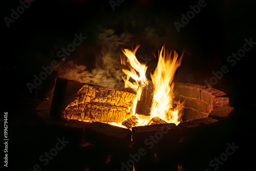 Big fire glows warm at night with bright flames and smoke in stone circle outside