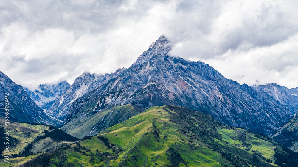 Fototapeta premium Landscape of Mount Genie and alpine grasslands in western Sichuan, China, with dramatic clouds, snow-capped peaks and changing light across the Tibetan Plateau.