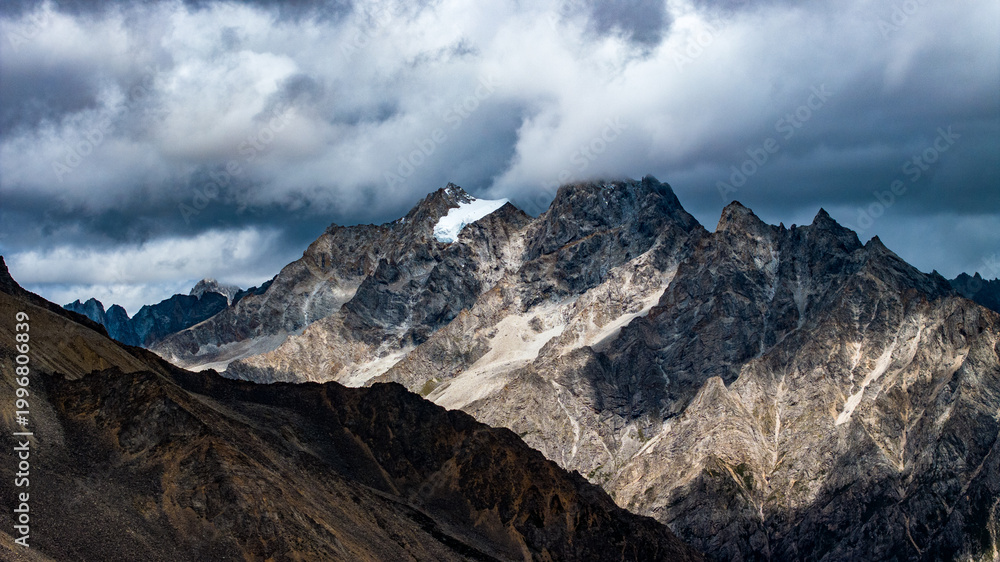 Obraz premium Landscape of Mount Genie and alpine grasslands in western Sichuan, China, with dramatic clouds, snow-capped peaks and changing light across the Tibetan Plateau.