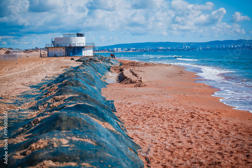 Sand dunes covered with protective blue netting on the beach after a storm. Coastal erosion, environmental protection and shore management concept