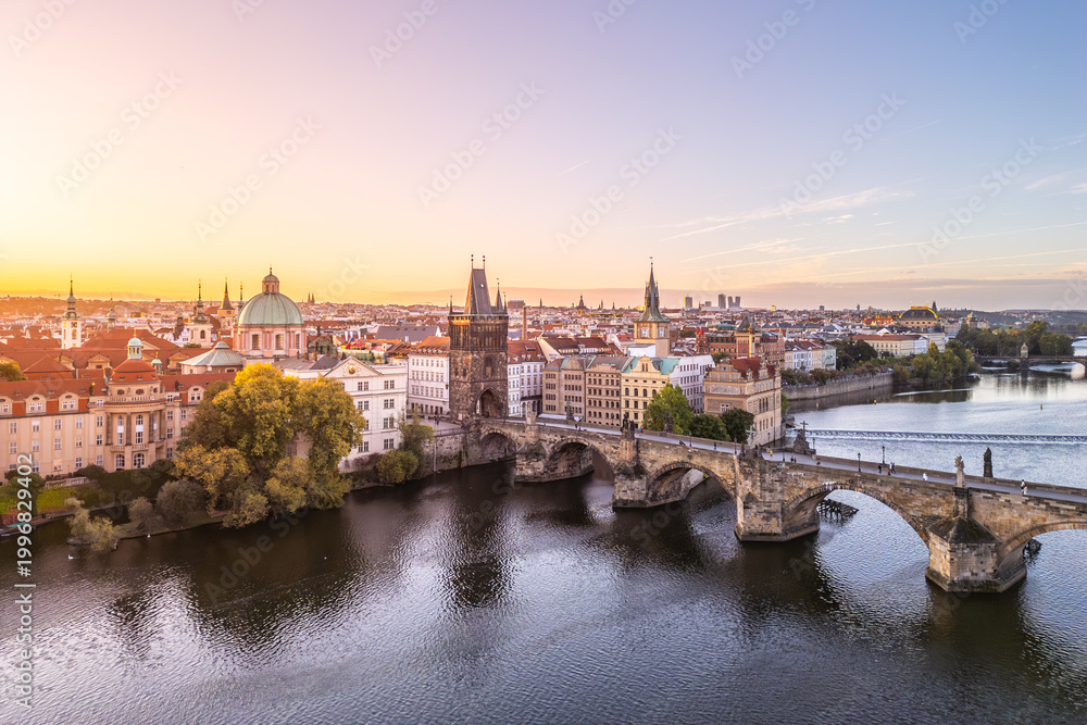 Fototapeta premium The Old Town Bridge Tower stands tall against a colorful sunset in Prague. The historic Charles Bridge stretches across the Vltava River, framed by city buildings.