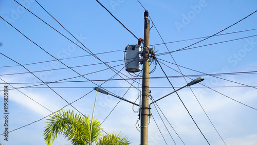 Concrete utility pole with cylindrical transformer, insulators, and multiple electrical wires extending outward.