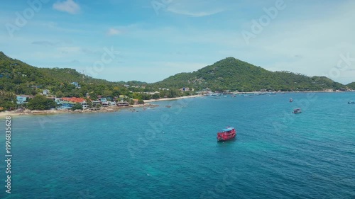 Vivid Red Boat Smoothly Sailing Towards Lively Seaside Community Nestled Among Green Hills