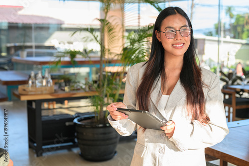 A professional Asian woman from Thai Isan looking away while holding a tablet in an authentic cafe