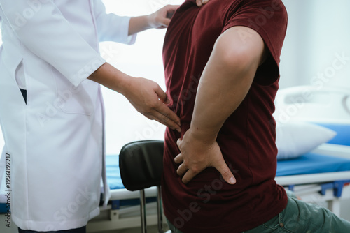 Billede på lærred Doctor explaining spine anatomy with a model to a male patient experiencing lower back pain in a clinic, discussing diagnosis and treatment options