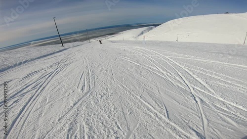 Crisscrossed Snow Field With Visible Ski Tracks, Gentle Hill And Distant Sea, Scattered Poles And Textured Snow Patterns, Recreational Freeride Atmosphere With Daytime Light And Panoramic View