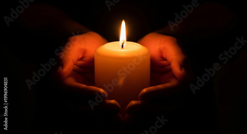 Candle in hands. Heart-shaped hands holding yellow candle in dark.