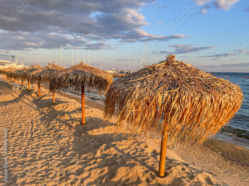 Row of straw beach umbrellas on sandy shore at sunset