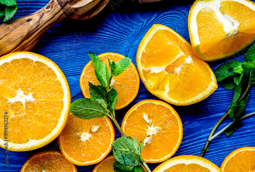 cut oranges with knife and mint leaves on blue kitchen top view