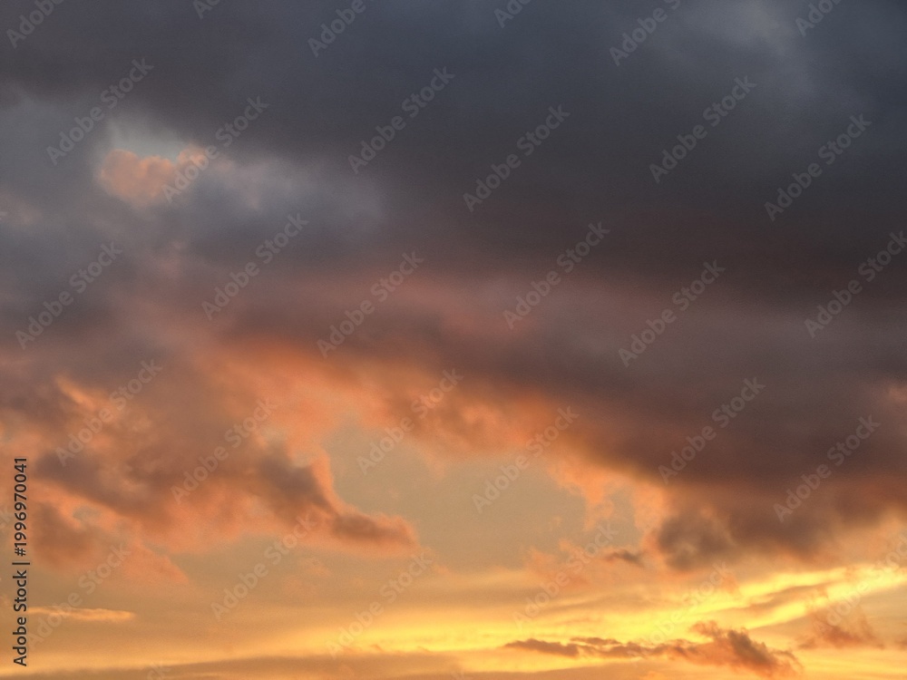 Fototapeta premium Dramatic sunset sky with glowing orange clouds and dark storm formations creating moody atmospheric background