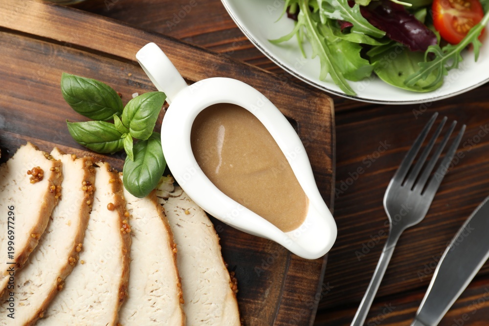 Naklejka premium Tasty turkey gravy in sauce boat, baked meat and salad on wooden table, flat lay