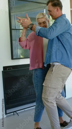 Vertical video: Linking hands, couple dancing at home near fireplace in denim and pink, connecting