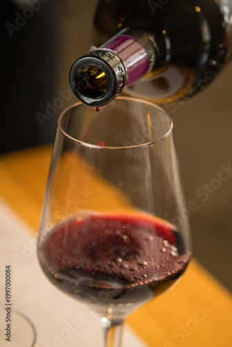 Sophisticated image capturing red wine being elegantly poured from a bottle into a clear glass by a server in a fine dining restaurant, set against a blurred background of a busy, atmospheric dining r
