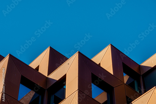 Geometric Form Architecture Shape Building Minimalist Abstract Urban Lines Exterior Featuring Sharp Angular Rooftops Symmetrical Patterns And Rhythmic Projections Under Clear Blue Sky