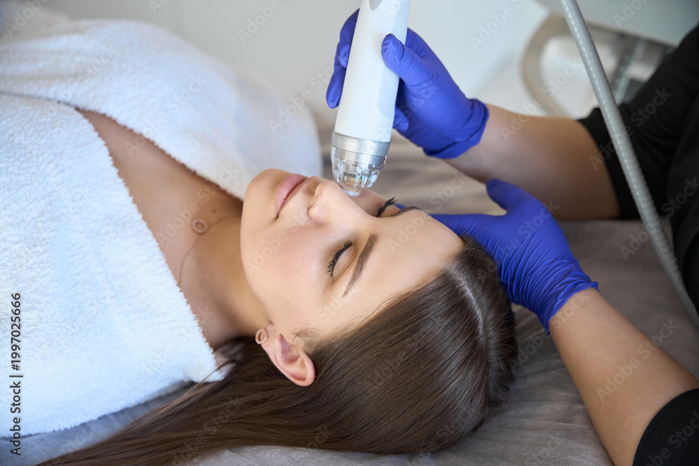 Fototapeta premium Cosmetologist making the RF lifting procedure for young lady in beauty salon