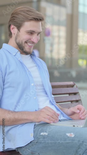 Man Celebrating Success on Laptop while Sitting Outdoor on Bench, Vertical Video