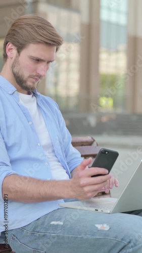 Man Using Smartphone and Laptop while Sitting Outdoor on Bench, Vertical Video