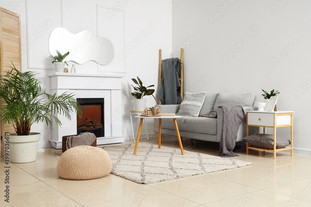 Obraz premium Interior of light living room with mirror, grey sofa and fireplace