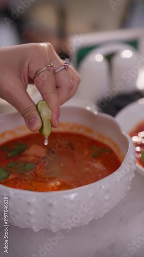 Female hand squeezing lime into tom yum soup in a bowl. Traditional Thai spicy soup served in a restaurant or at home