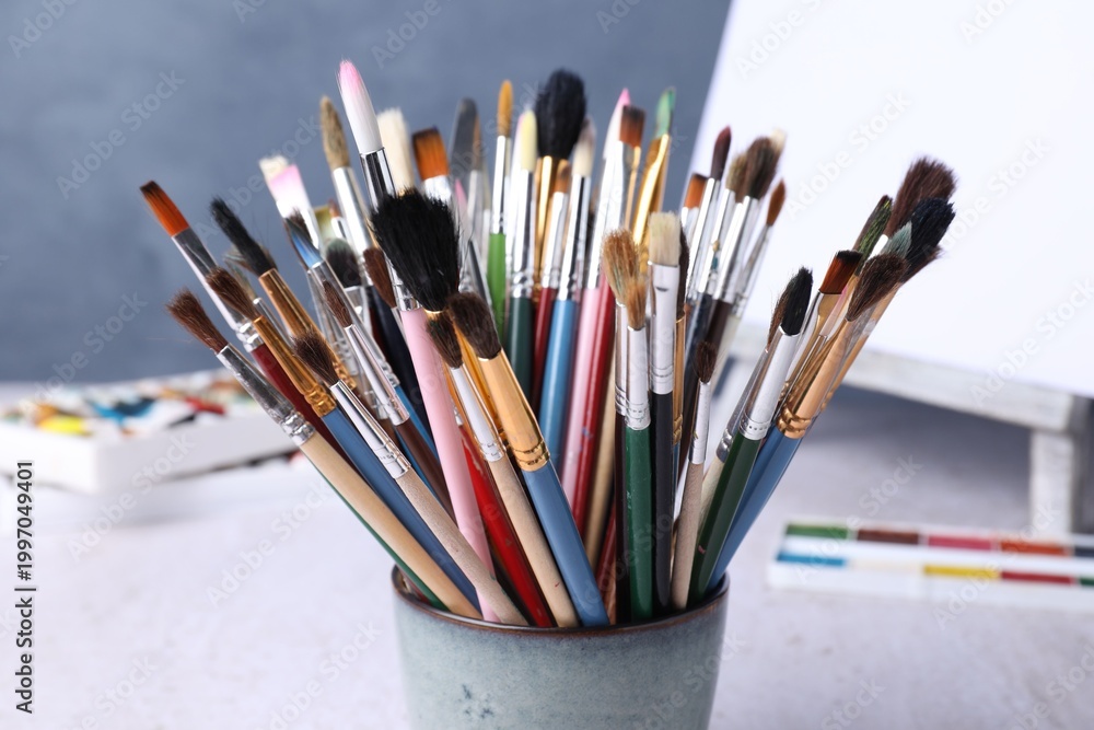 Fototapeta premium Paintbrushes, paints and easel with canvas on table near blue wall, closeup