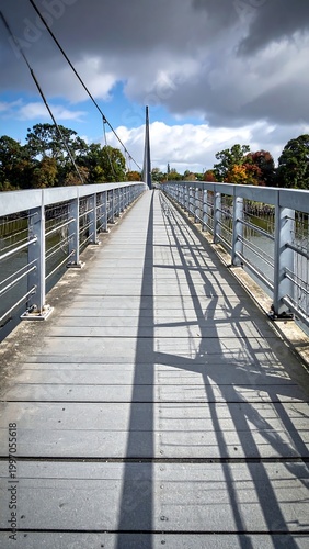 Elevated view of a metal pedestrian bridge stretching into the distance under a partly cloudy sky, with tall trees